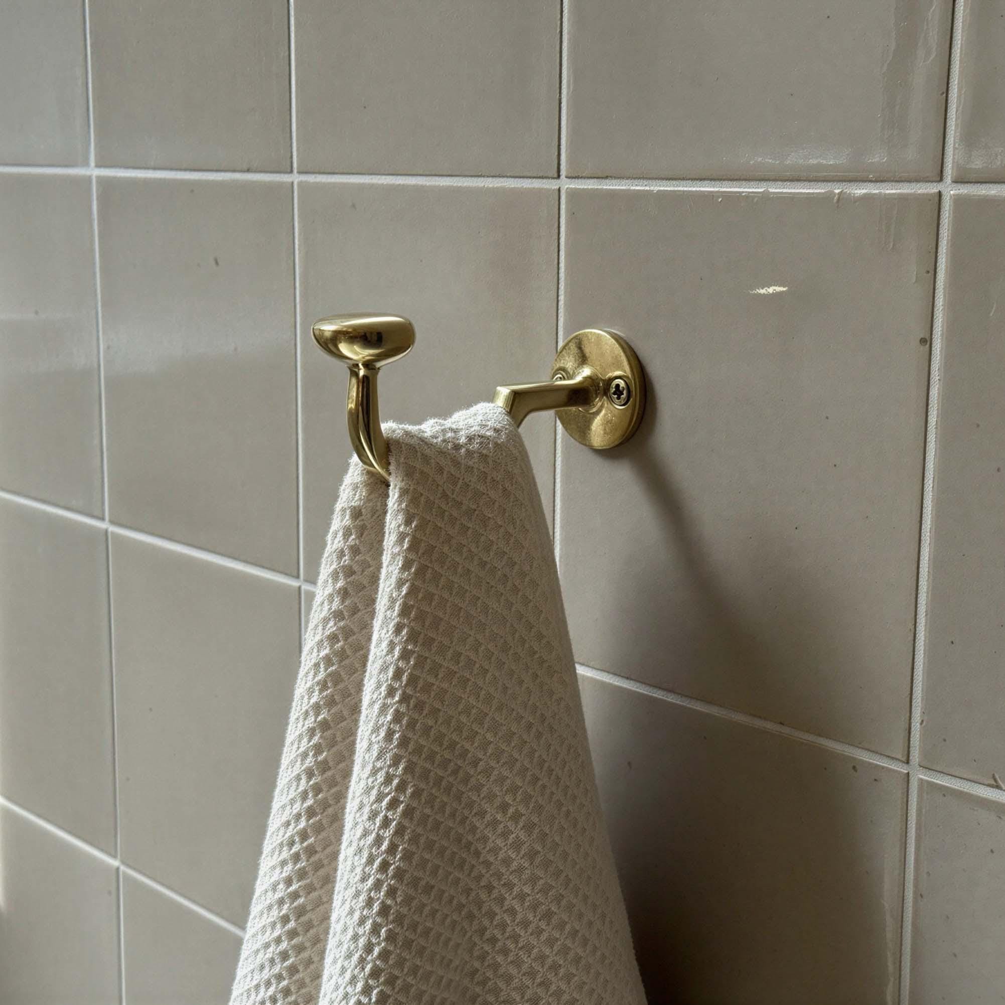 Gold towel hook with a white towel on a tiled bathroom wall