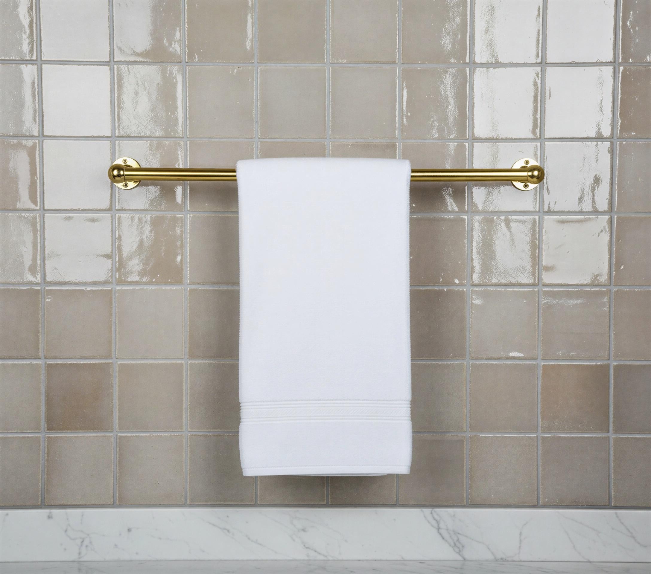 White towel hanging on a gold towel rack against a tiled bathroom wall.
