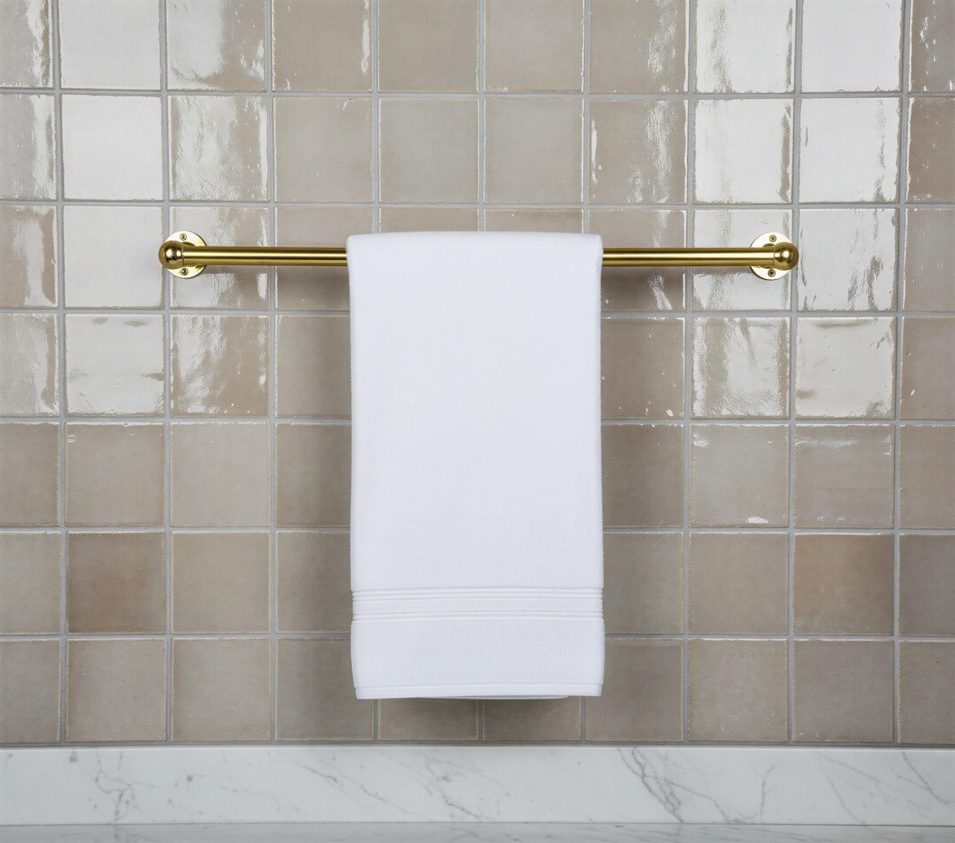 White towel hanging on a gold towel rack against a tiled bathroom wall.