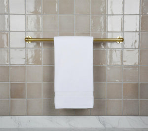 White towel hanging on a gold towel rack against a tiled bathroom wall.