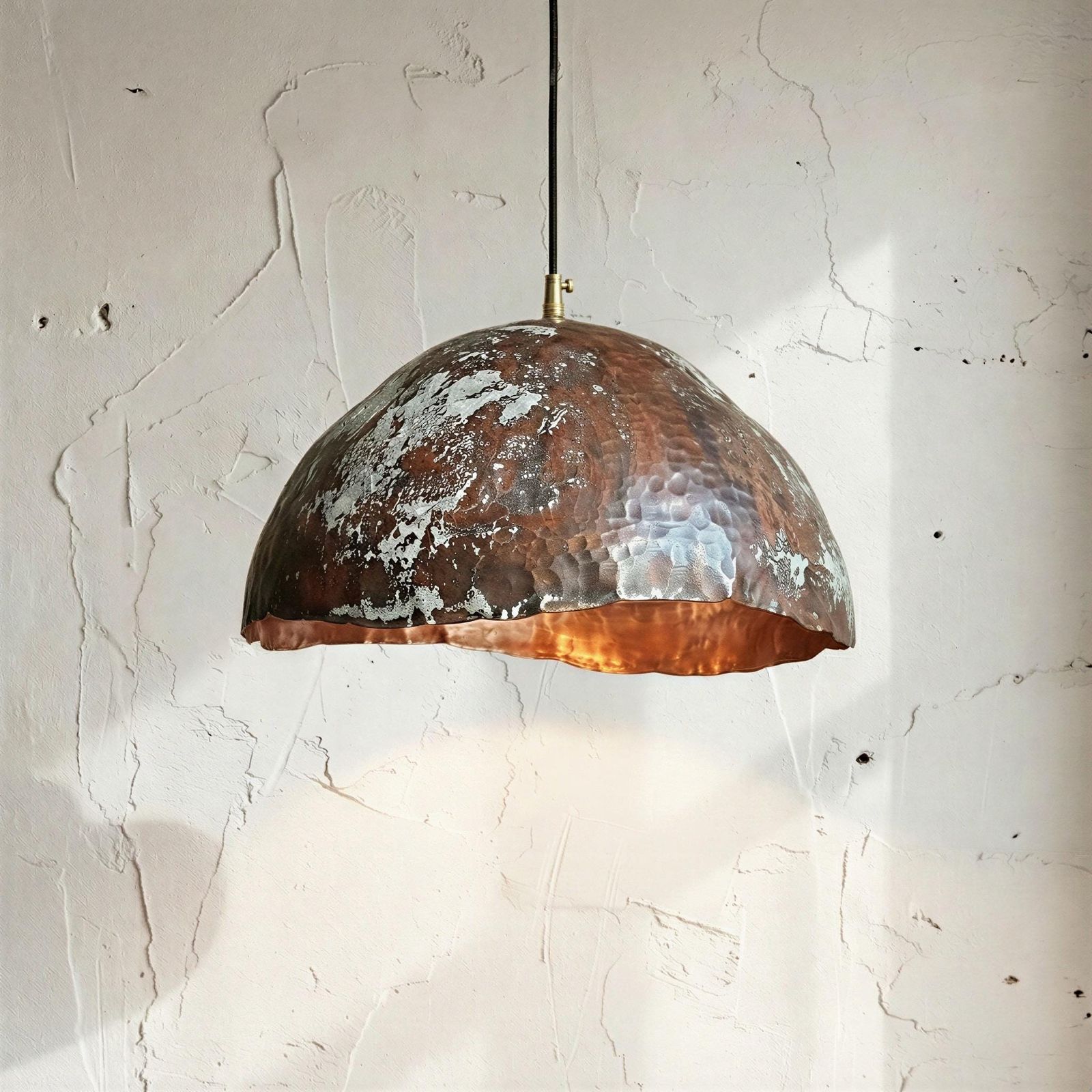 Copper pendant light hanging against a textured white wall