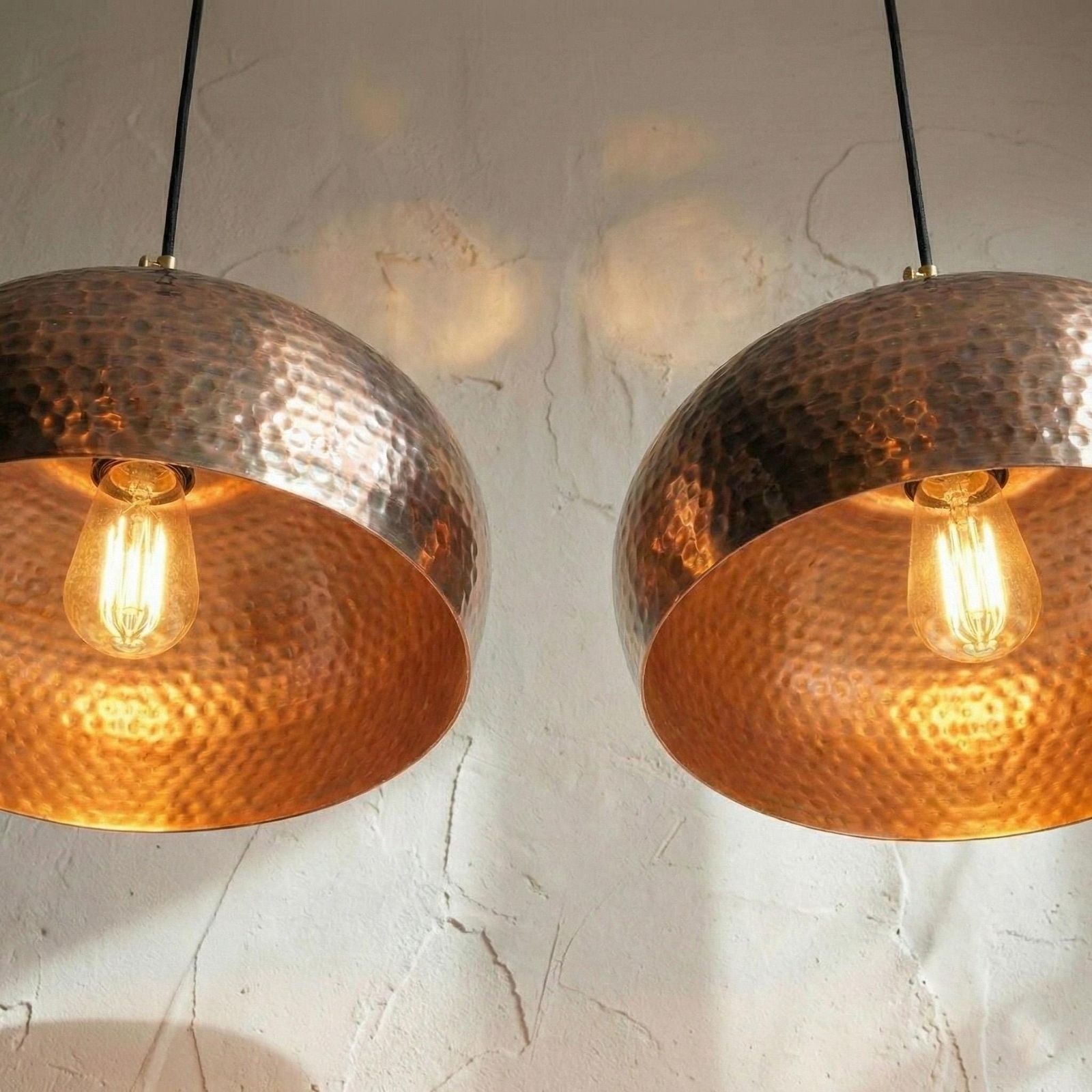 Two copper pendant lights hanging against a textured white wall.