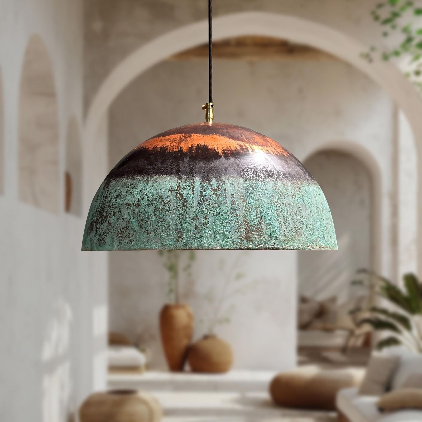 A dome-shaped pendant light with a distressed, multi-toned metallic finish featuring orange, dark brown, and turquoise-green hues, hanging in a softly blurred, warm-toned interior setting.