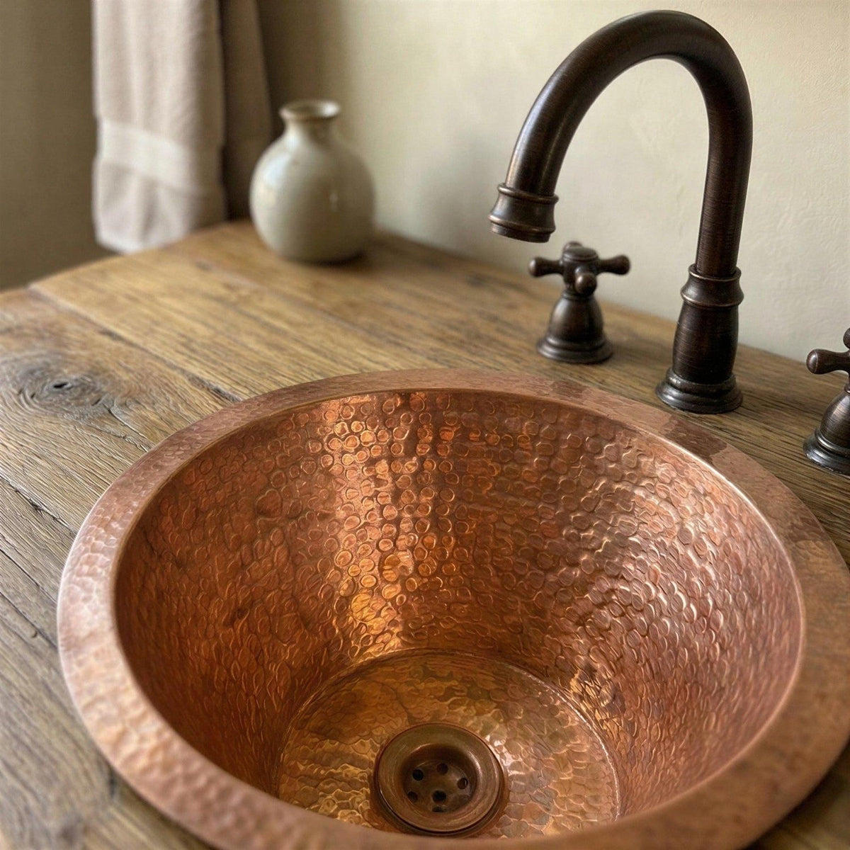 Copper sink with textured surface and dark faucet on a wooden countertop.