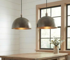 Two metallic pendant lights hanging above a wooden table with a window in the background.