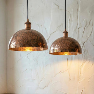 Two copper pendant lights hanging against a textured white wall.