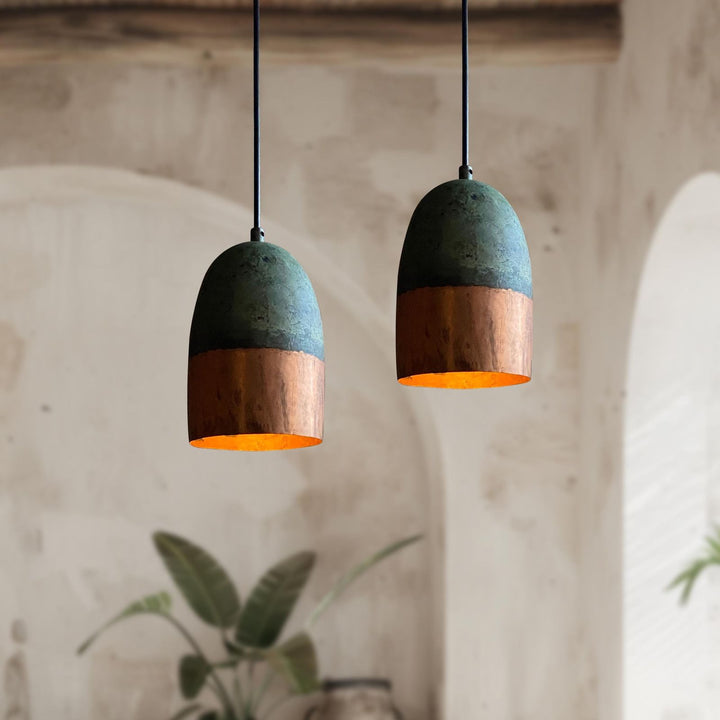 Two pendant lights with green and copper design hanging against a neutral wall.