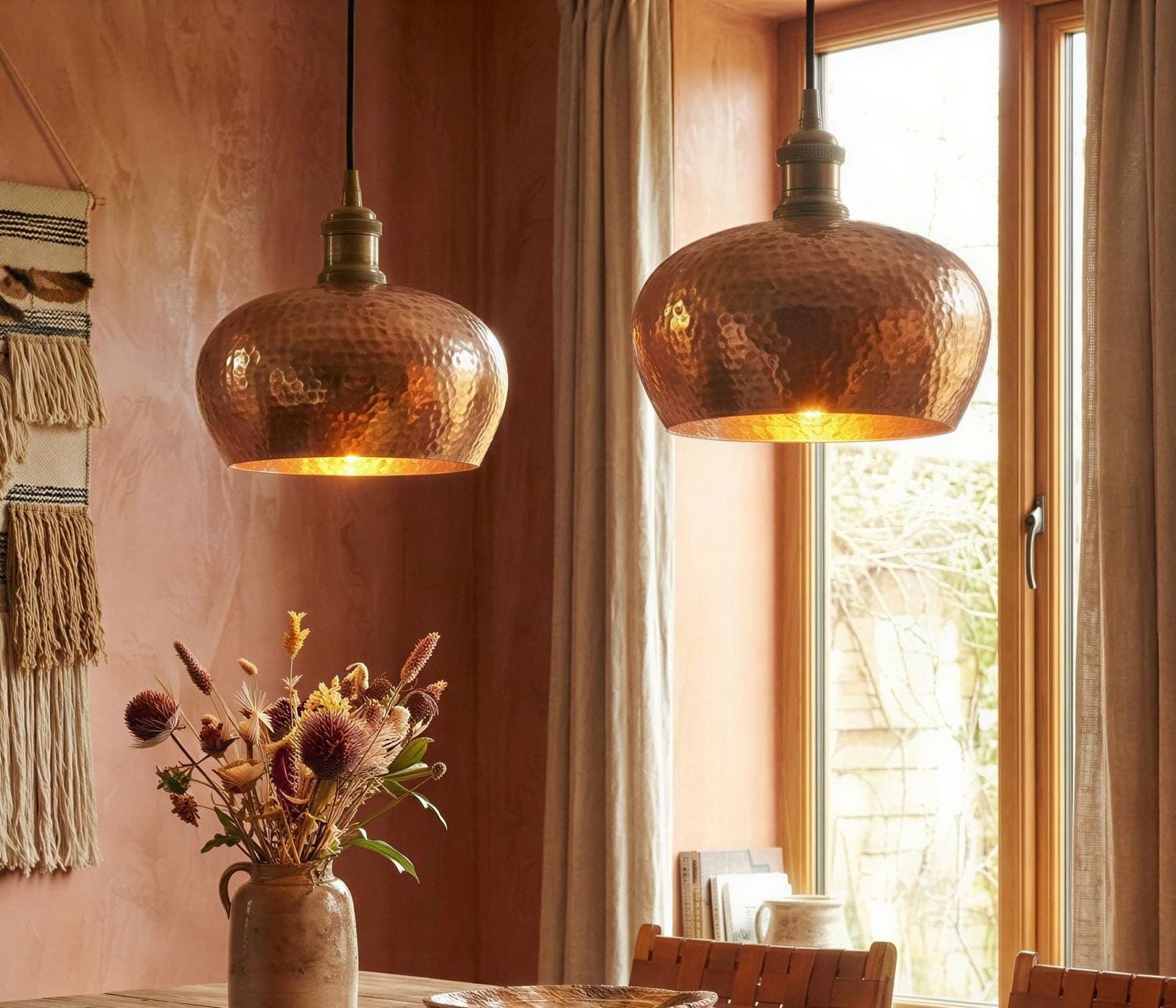 Two copper pendant lights hanging above a dining table with a vase of flowers.