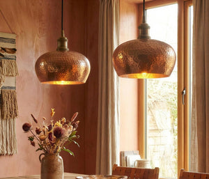 Two copper pendant lights hanging above a dining table with a vase of flowers.