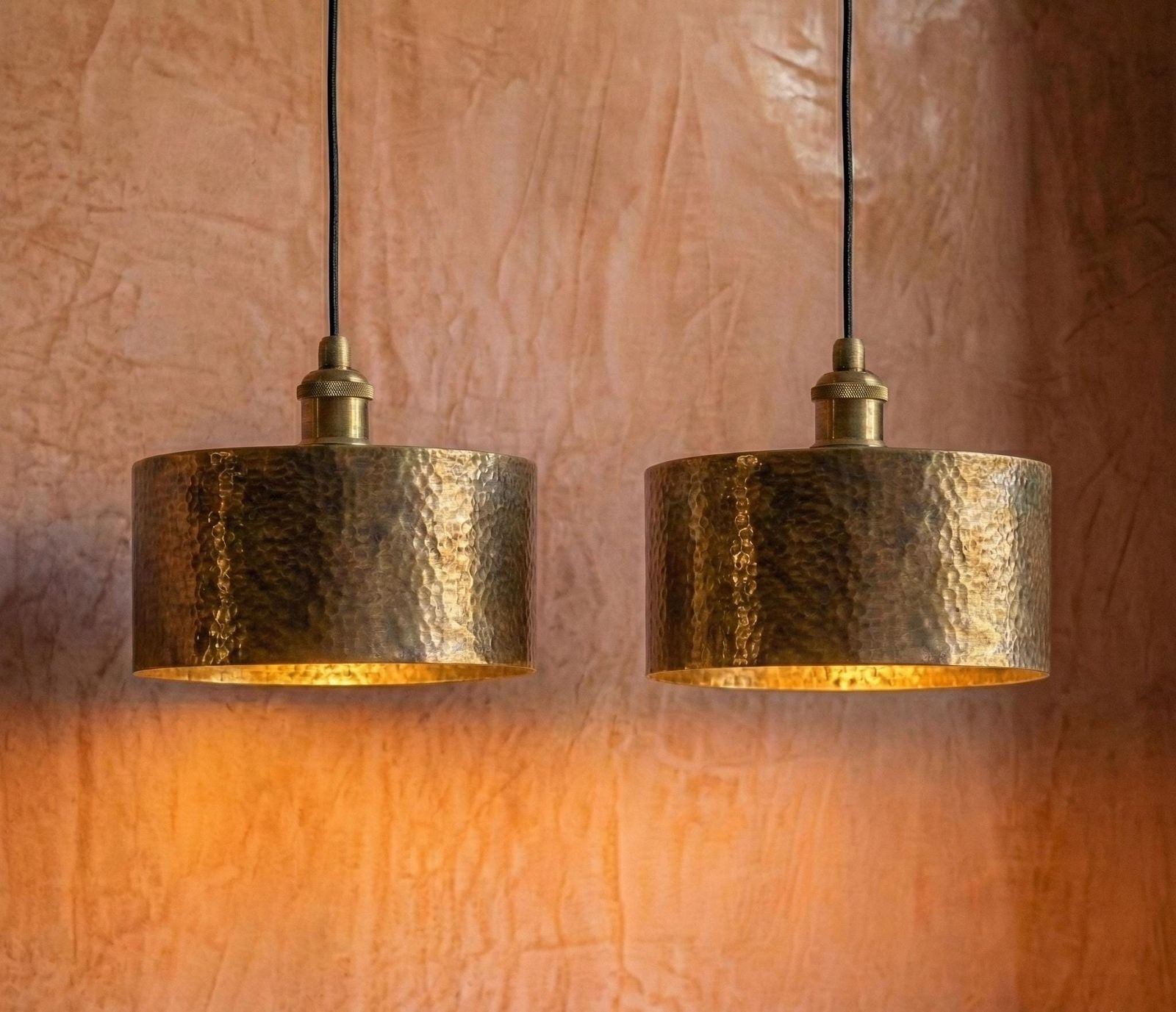 Two gold pendant lights hanging against a textured pink wall.