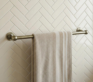 Towel hanging on a towel rack against a tiled wall with a herringbone pattern.