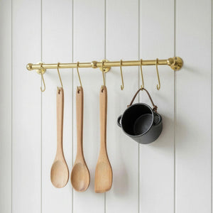 Wooden spoons and a black pot hanging on a brass rod against a white paneled wall.