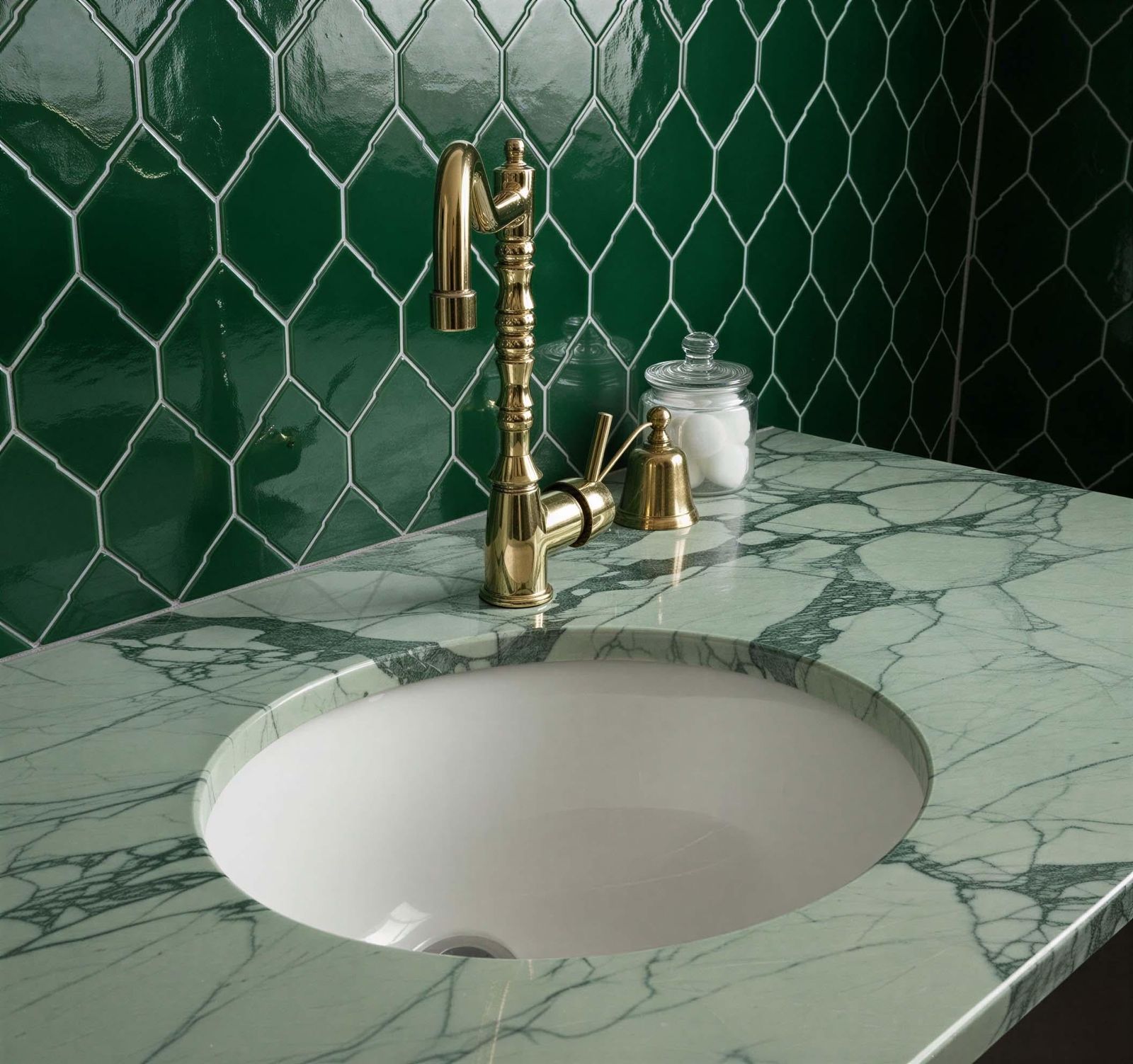 Bathroom sink with gold faucet against a green tiled wall