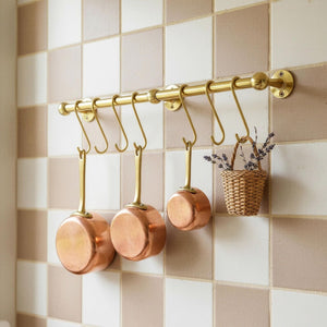 Copper pots hanging on a gold rod against a tiled wall
