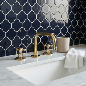 Bathroom with gold faucet and fixtures against a dark blue tiled wall.