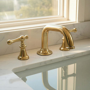 Gold bathroom faucet set on a marble countertop with a window in the background