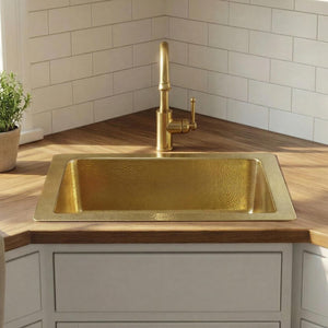 Gold kitchen sink in a modern kitchen with wooden countertops and white cabinets.