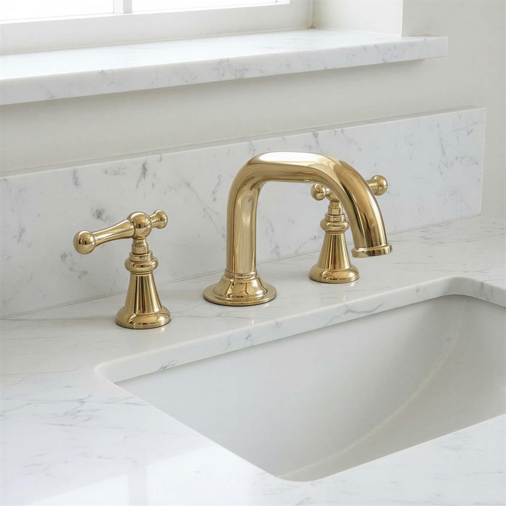 Gold faucet set on a marble countertop with a window in the background