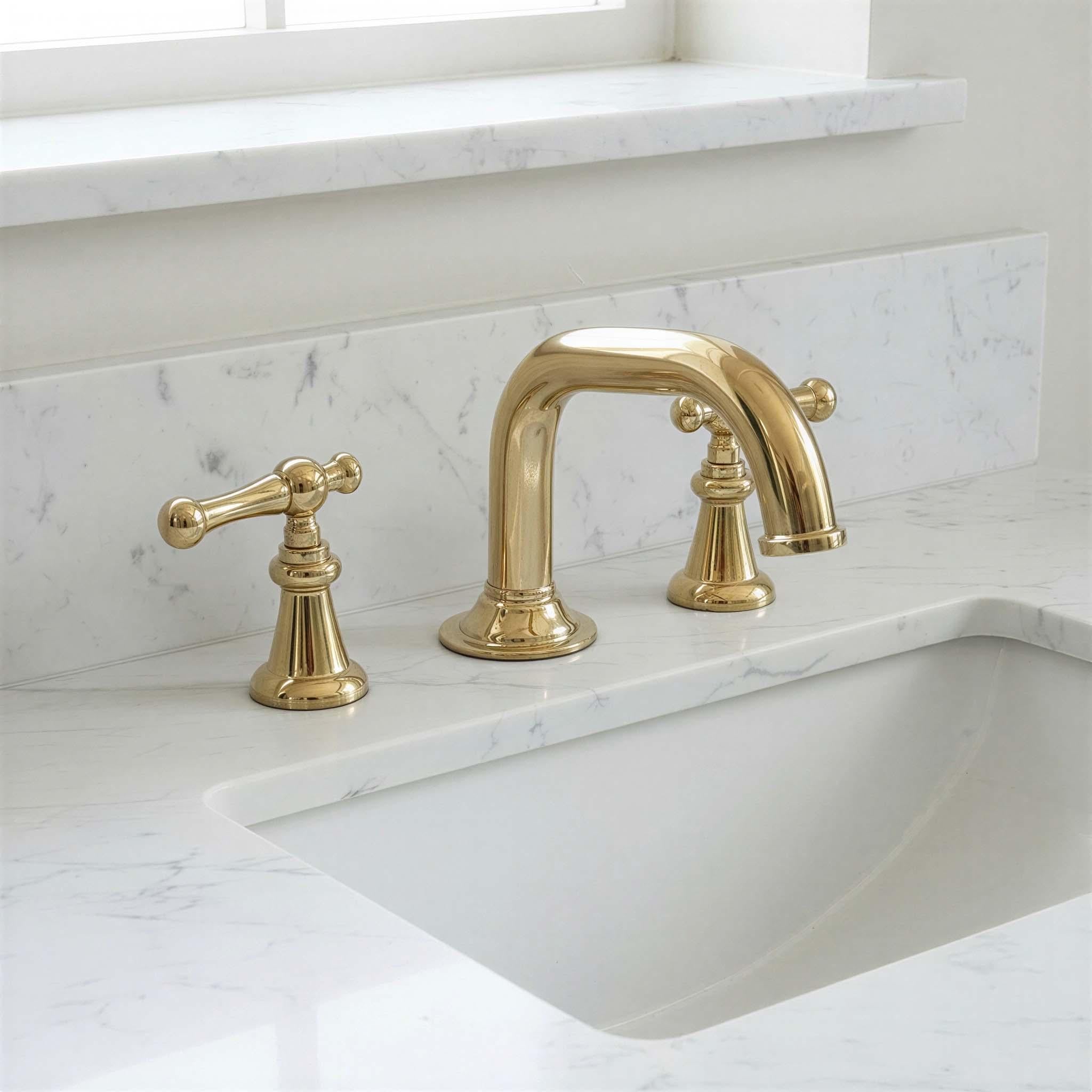 Gold faucet set on a marble countertop with a window in the background