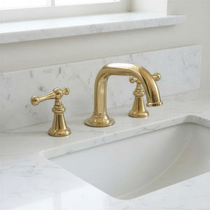 Gold faucet set on a marble countertop with a window in the background