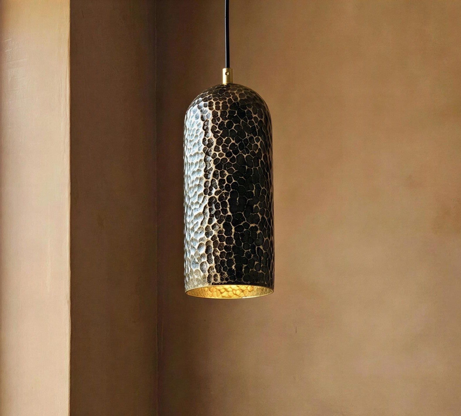 Hammered metal pendant light against a brown wall