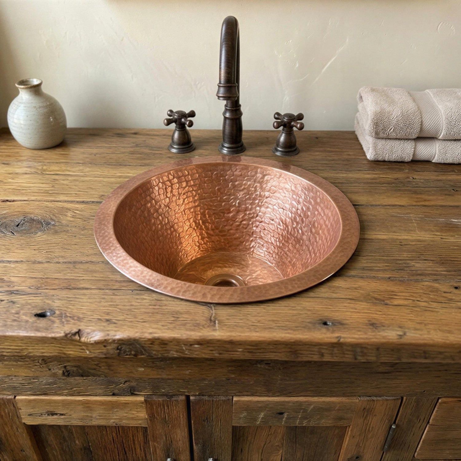 Copper sink on a wooden vanity with a faucet and towels in the background.