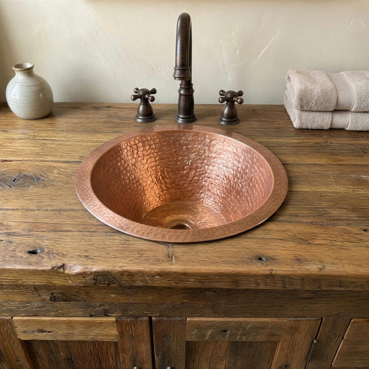 Copper sink on a wooden vanity with a faucet and towels in the background.