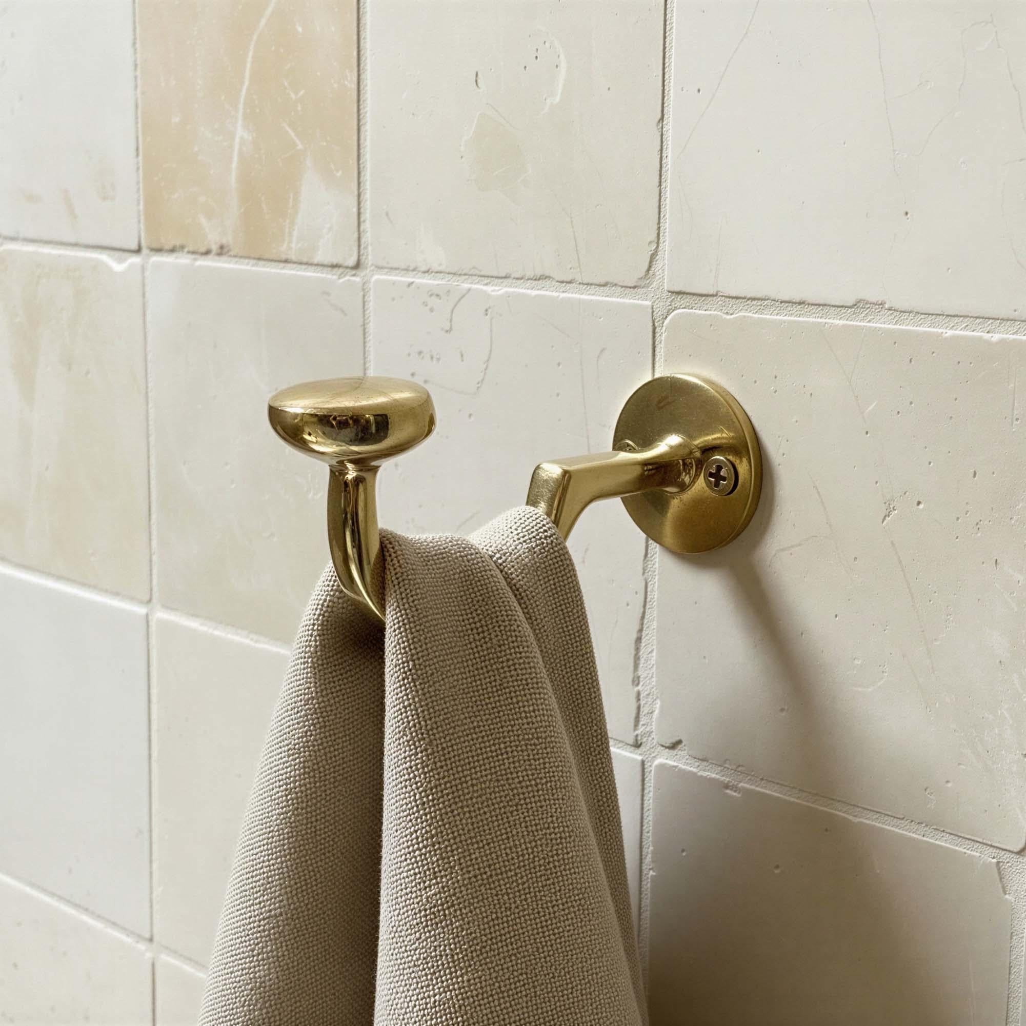 Gold towel hook on a tiled bathroom wall with a beige towel draped over it.