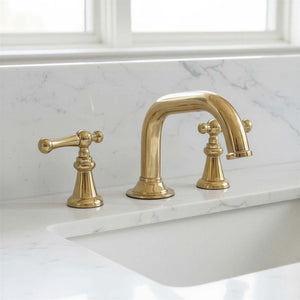 Gold faucet set on a marble countertop with a window in the background