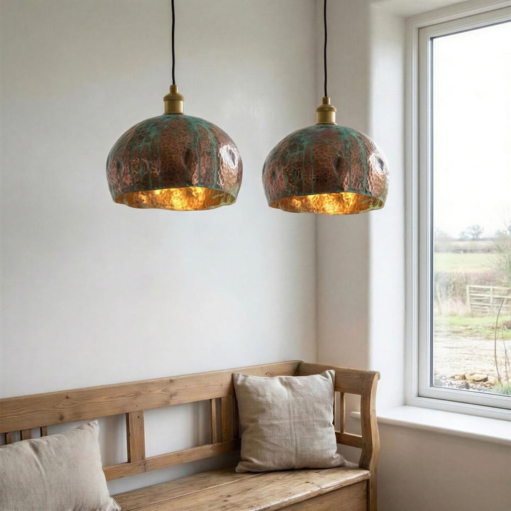 Two copper pendant lights hanging above a wooden bench with pillows in a room with a window.