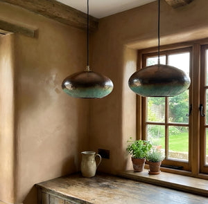 Two metallic pendant lights hanging above a wooden window sill with plants and a mug.