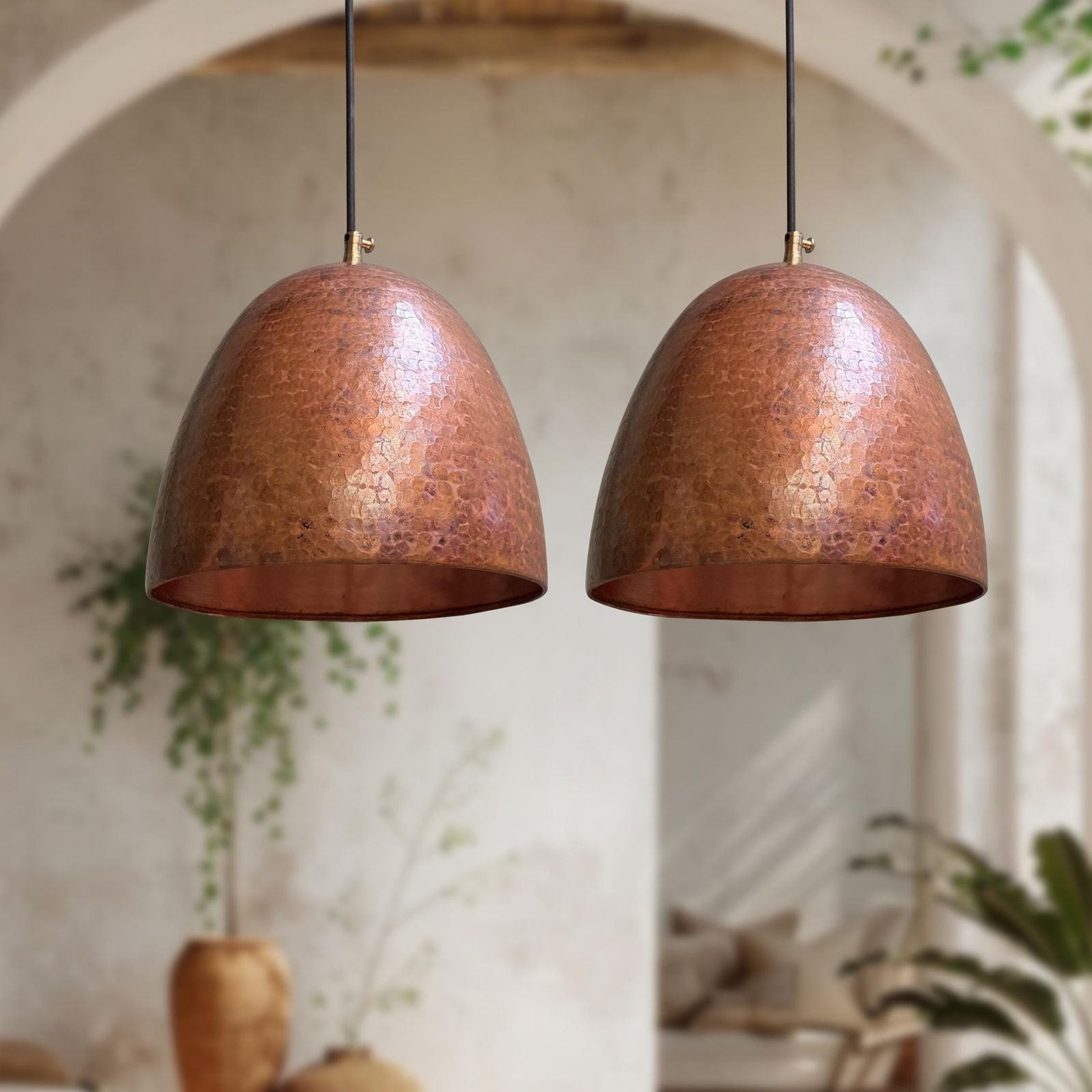 Two copper pendant lights hanging against a blurred indoor background with plants.