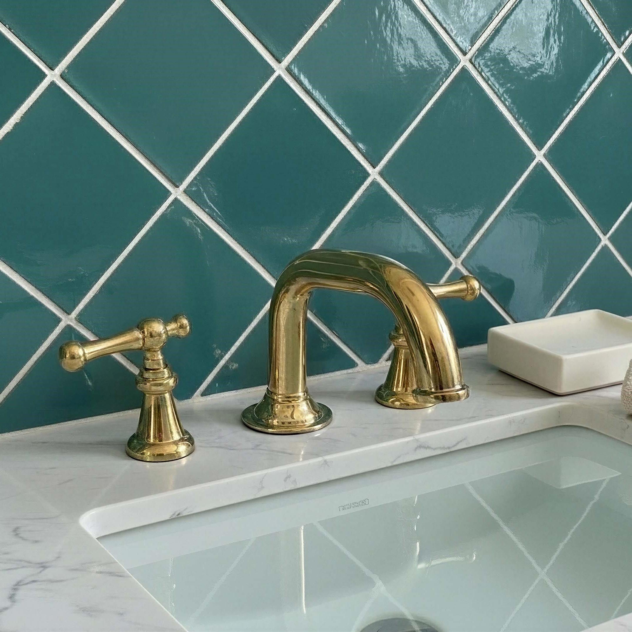 Gold faucet and handles on a marble countertop with teal tiled wall