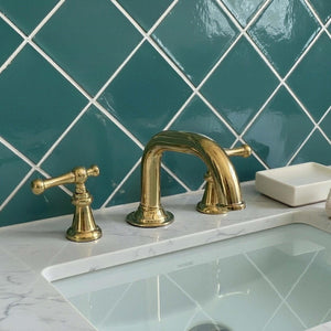 Gold faucet and handles on a marble countertop with teal tiled wall