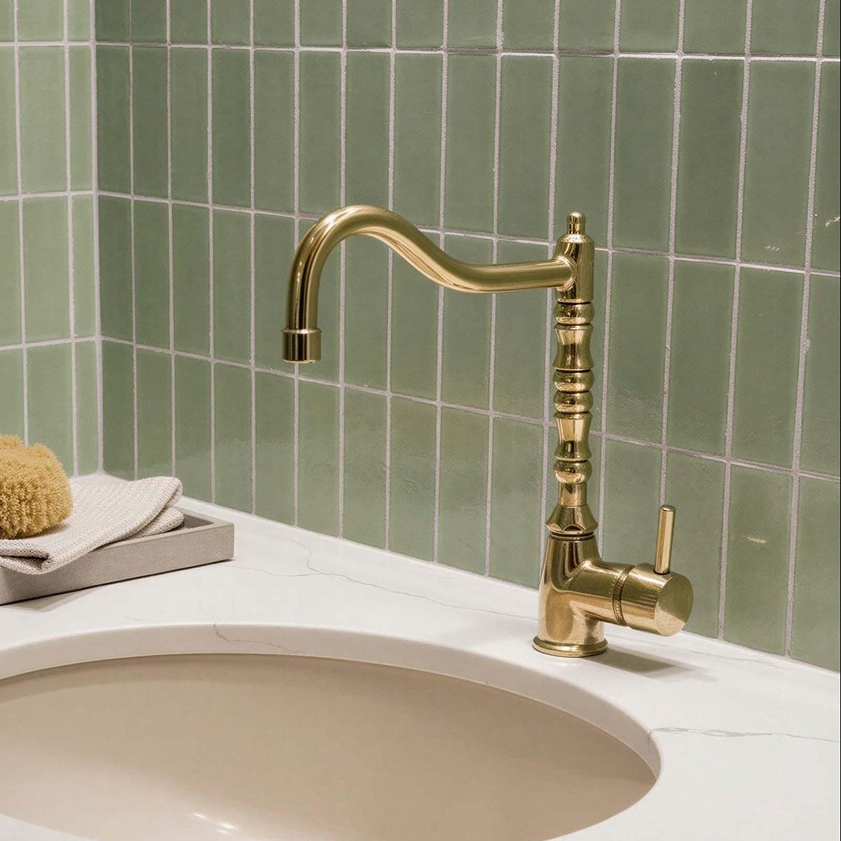 Bathroom sink with gold faucet against a green tiled wall