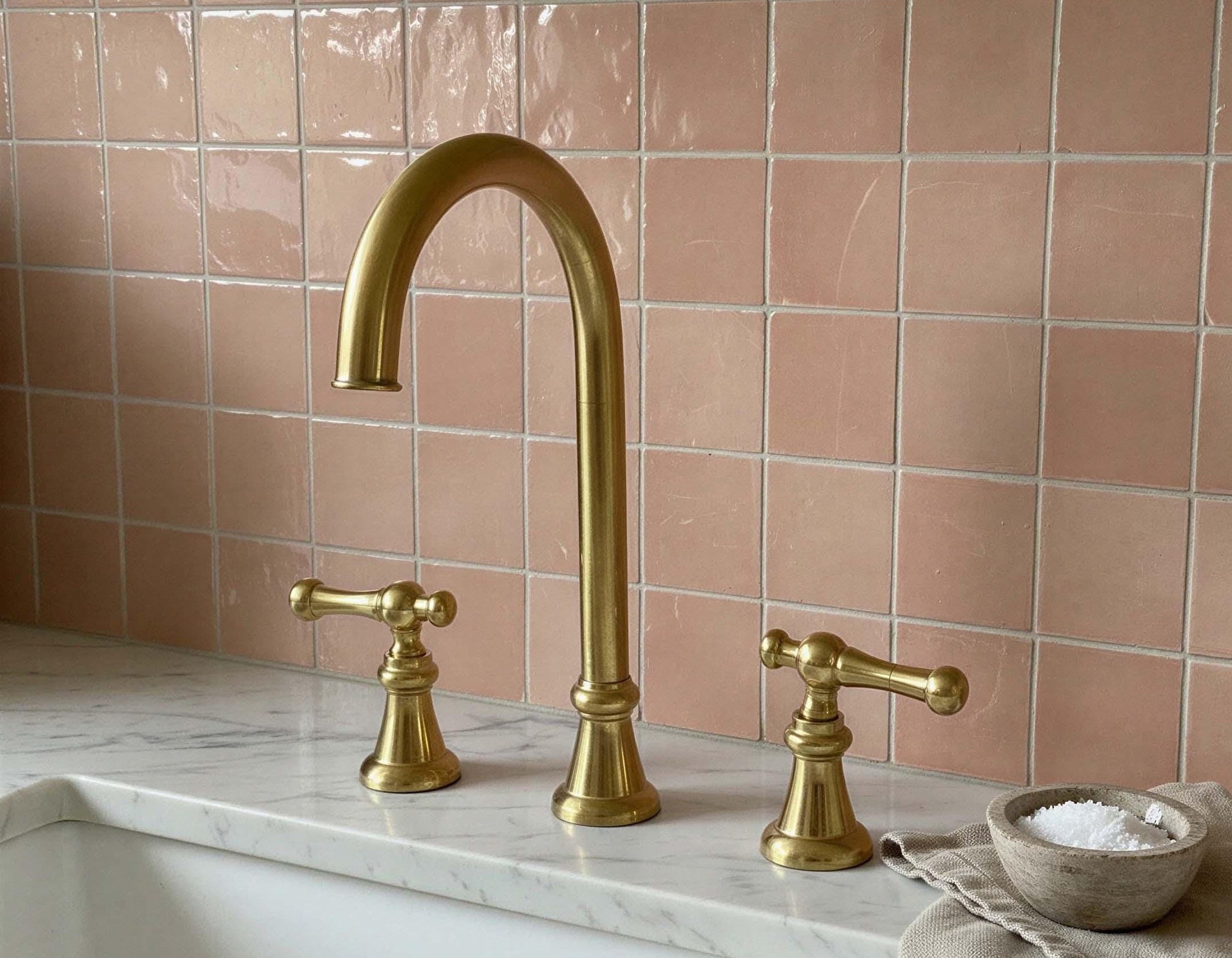 Gold faucet and handles on a marble countertop with pink tiled wall
