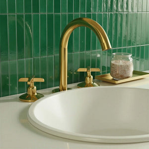 Gold faucet and handles on a white sink with green tiled wall