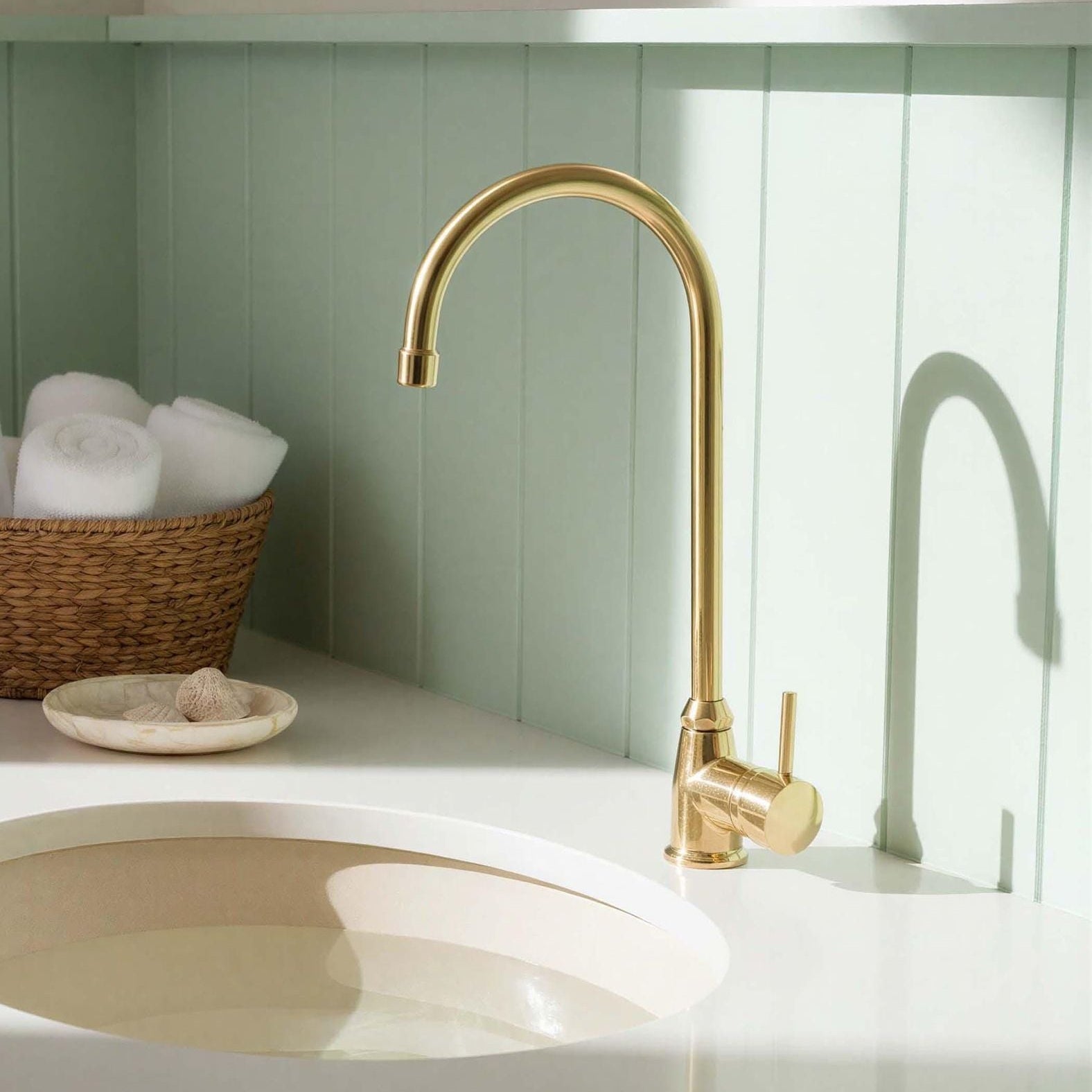 Gold kitchen faucet on a white countertop with a green wall in the background