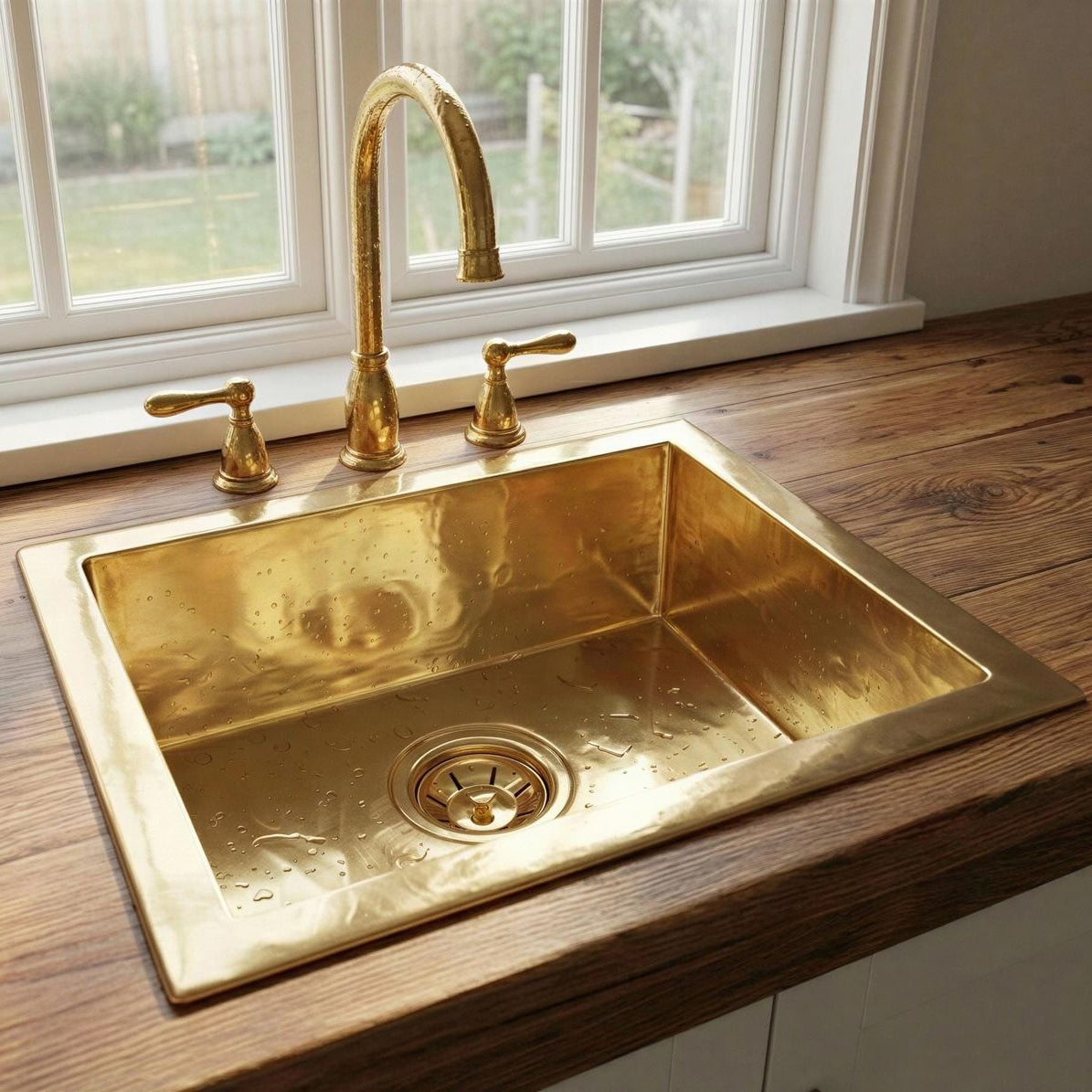 Gold kitchen sink with faucet on a wooden countertop near a window.