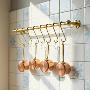 Set of copper pots hanging on a gold rack against a tiled wall.
