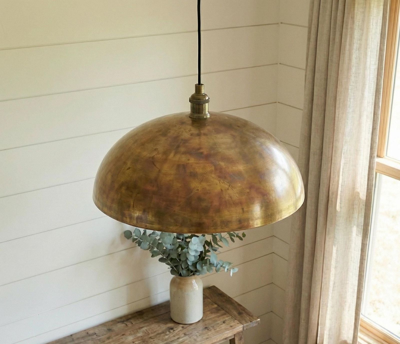 Brass pendant light hanging above a wooden surface with a vase of eucalyptus.