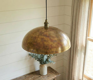 Brass pendant light hanging above a wooden surface with a vase of eucalyptus.