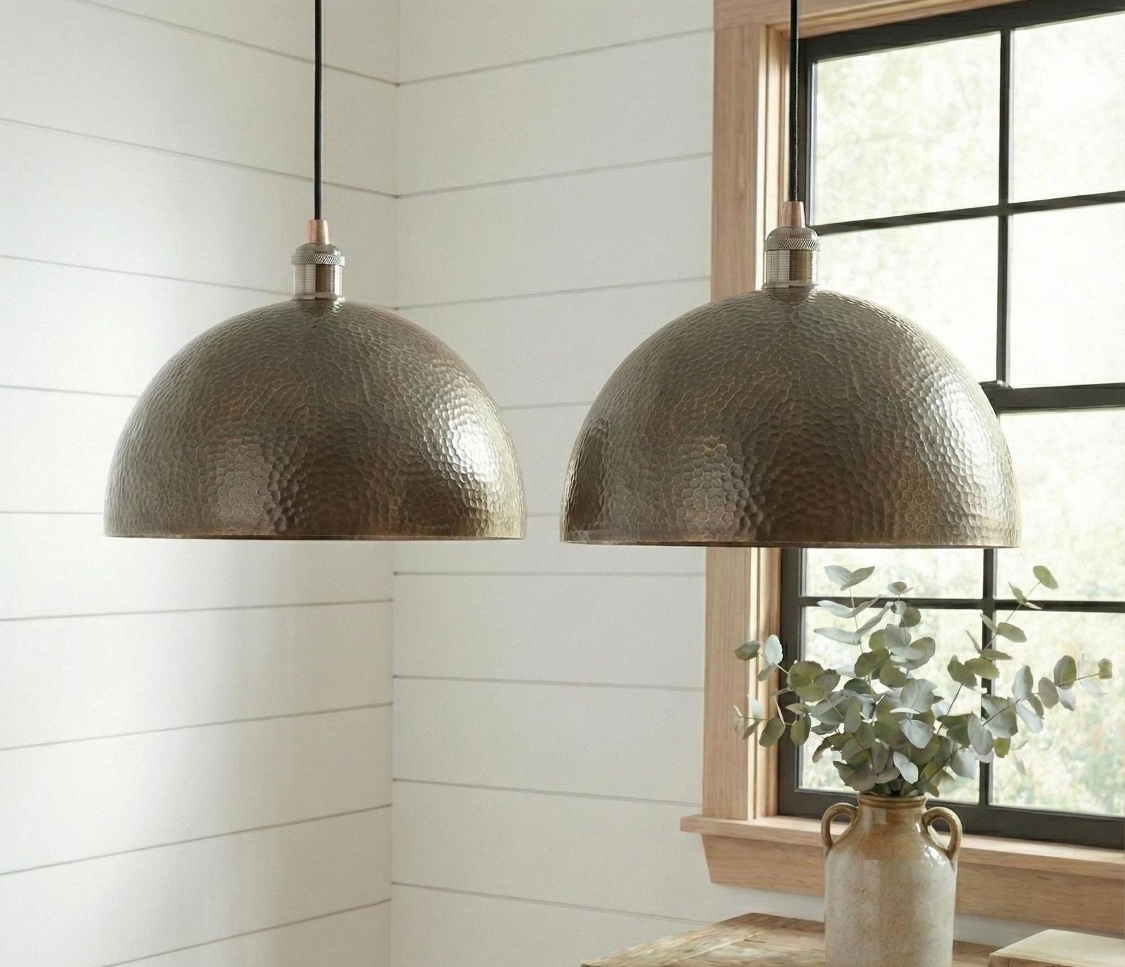 Two bronze dome pendant lights hanging in a room with a window and plant.