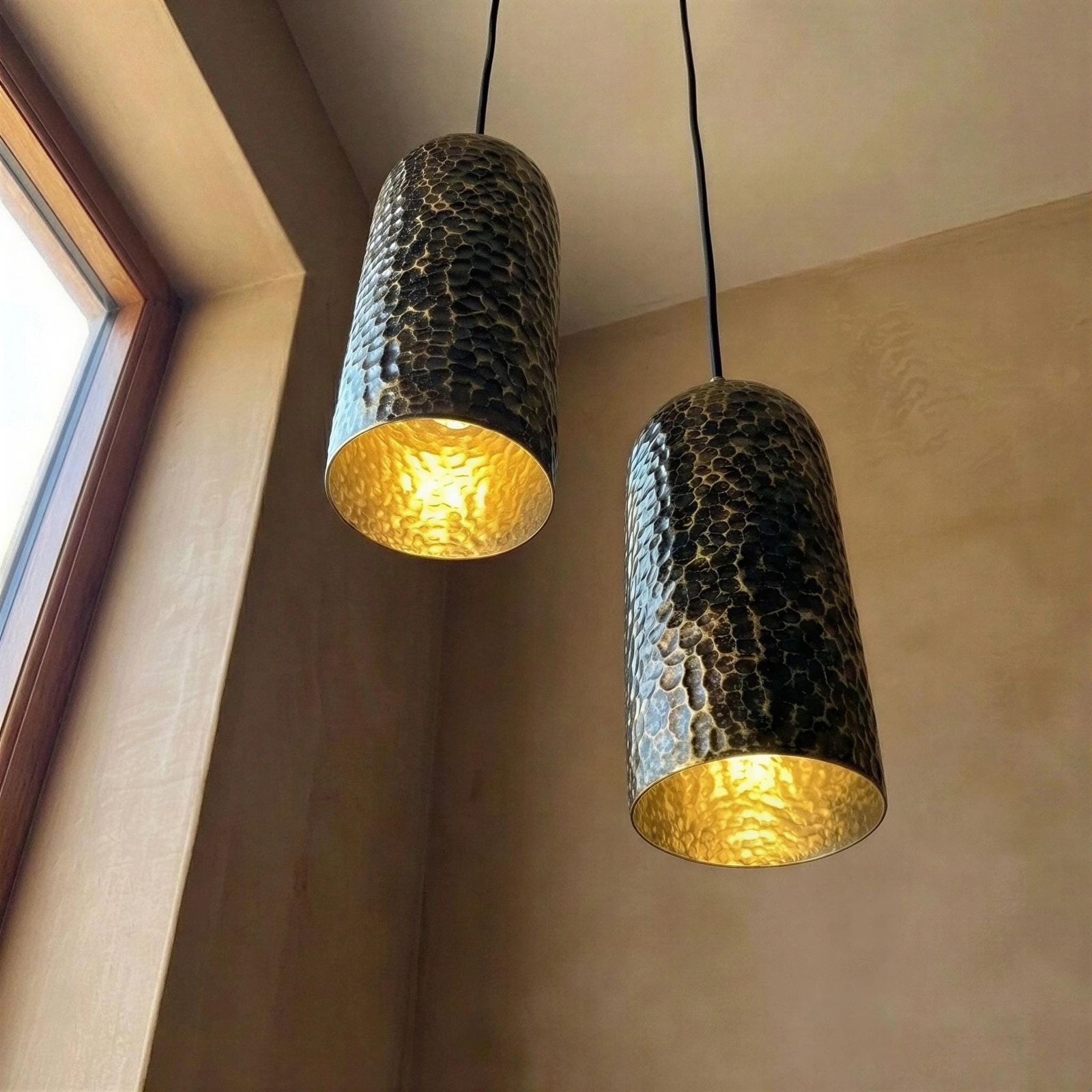 Two pendant lights with textured design and gold interior, hanging in a room with a window.