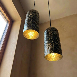 Two pendant lights with textured design and gold interior, hanging in a room with a window.