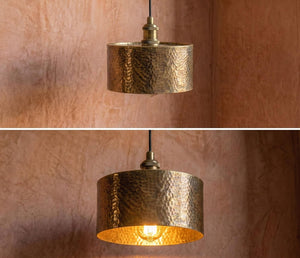 Hammered gold pendant light fixture on a textured brown wall.