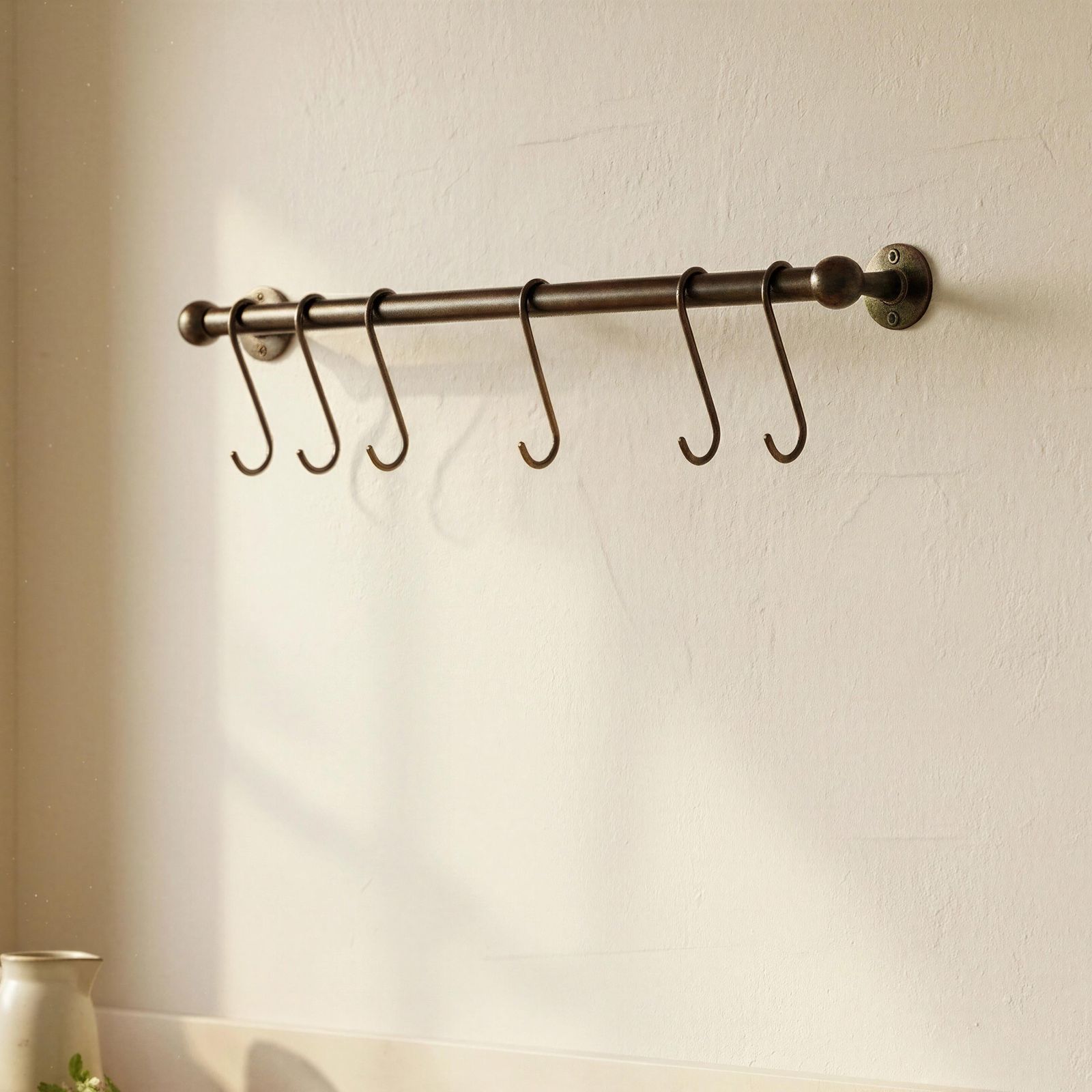 Wall-mounted metal rack with hooks on a light-colored wall