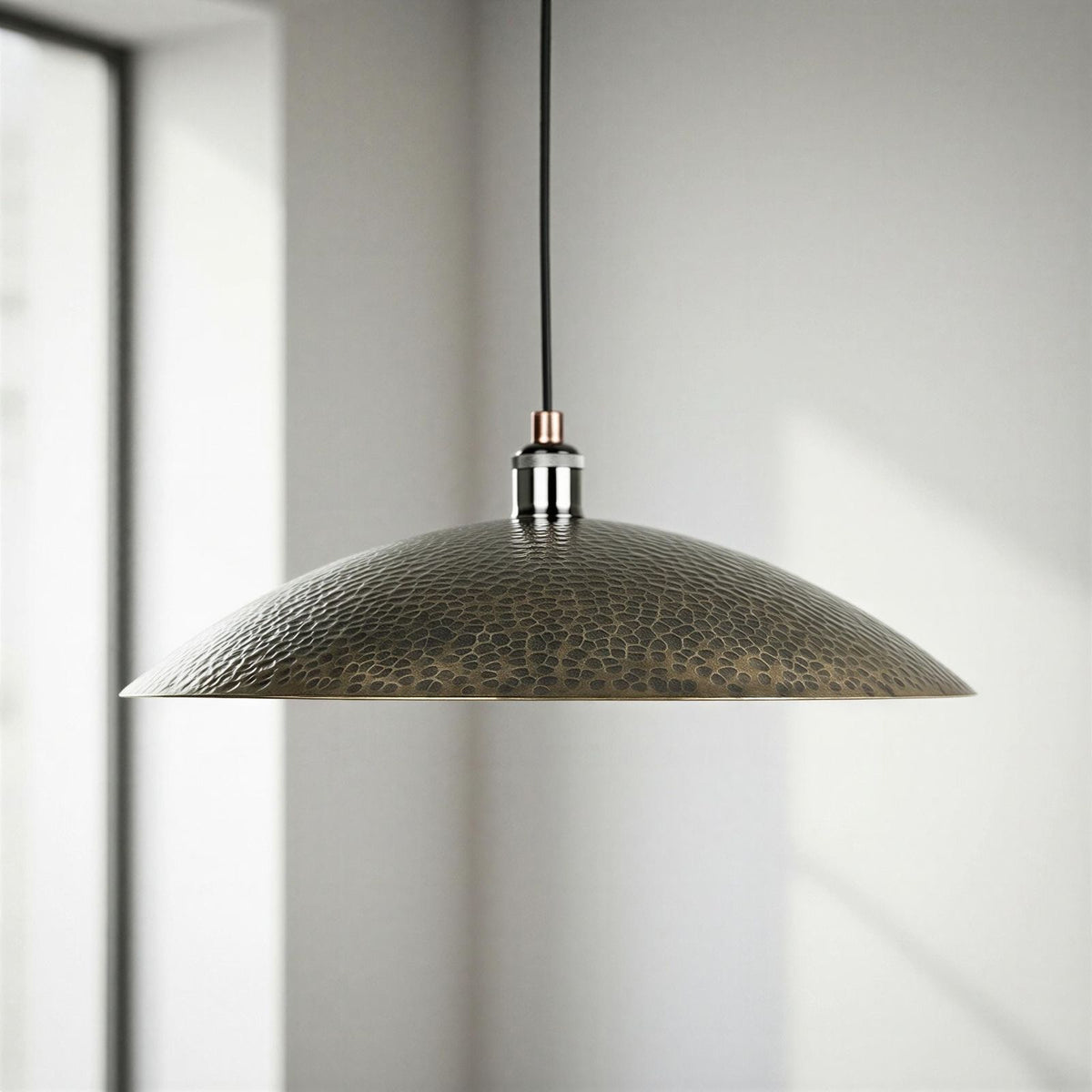 Hammered metal pendant light hanging in a room with a window.