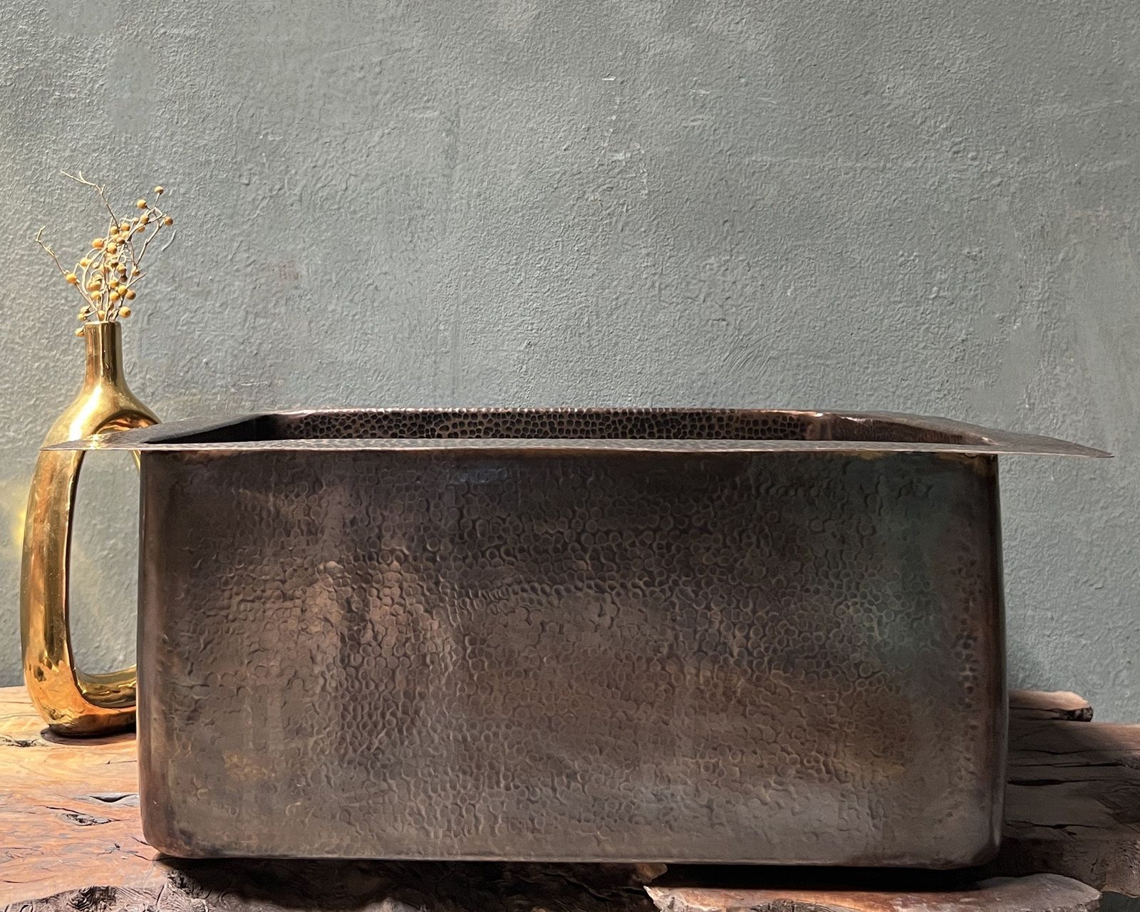 Rustic metal basin on a wooden surface with a textured gray wall background