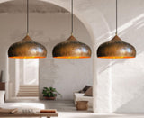 Three bronze dome pendant lights with a hammered metallic finish hang in a row over a modern, minimalist living room with white walls and arches.